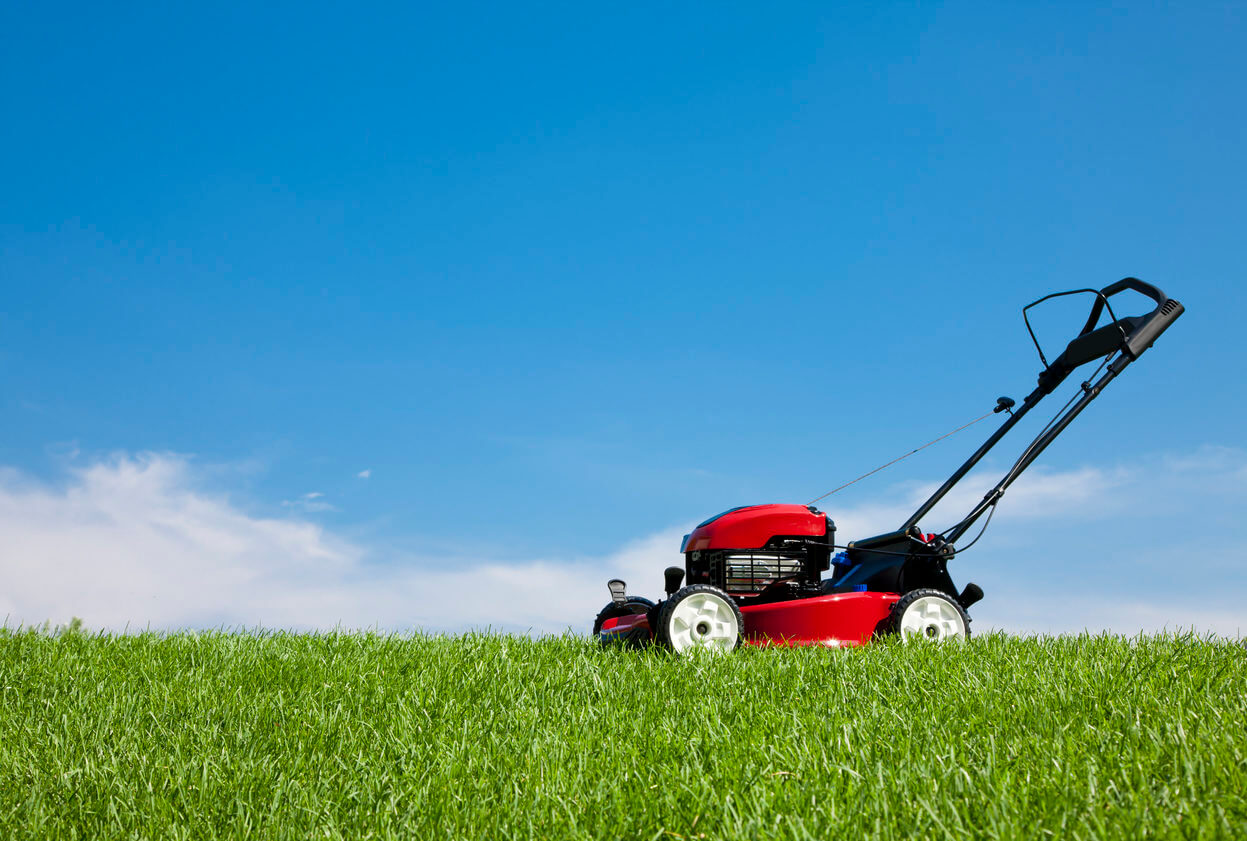 Lawn mower on lush green grass on a summer day under a blue sky.