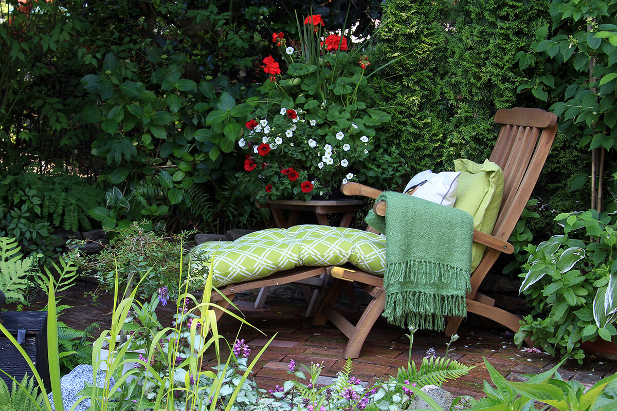 A comfortable lounge chair in a secluded garden area, enclosed by greenery and container plants and flowers.