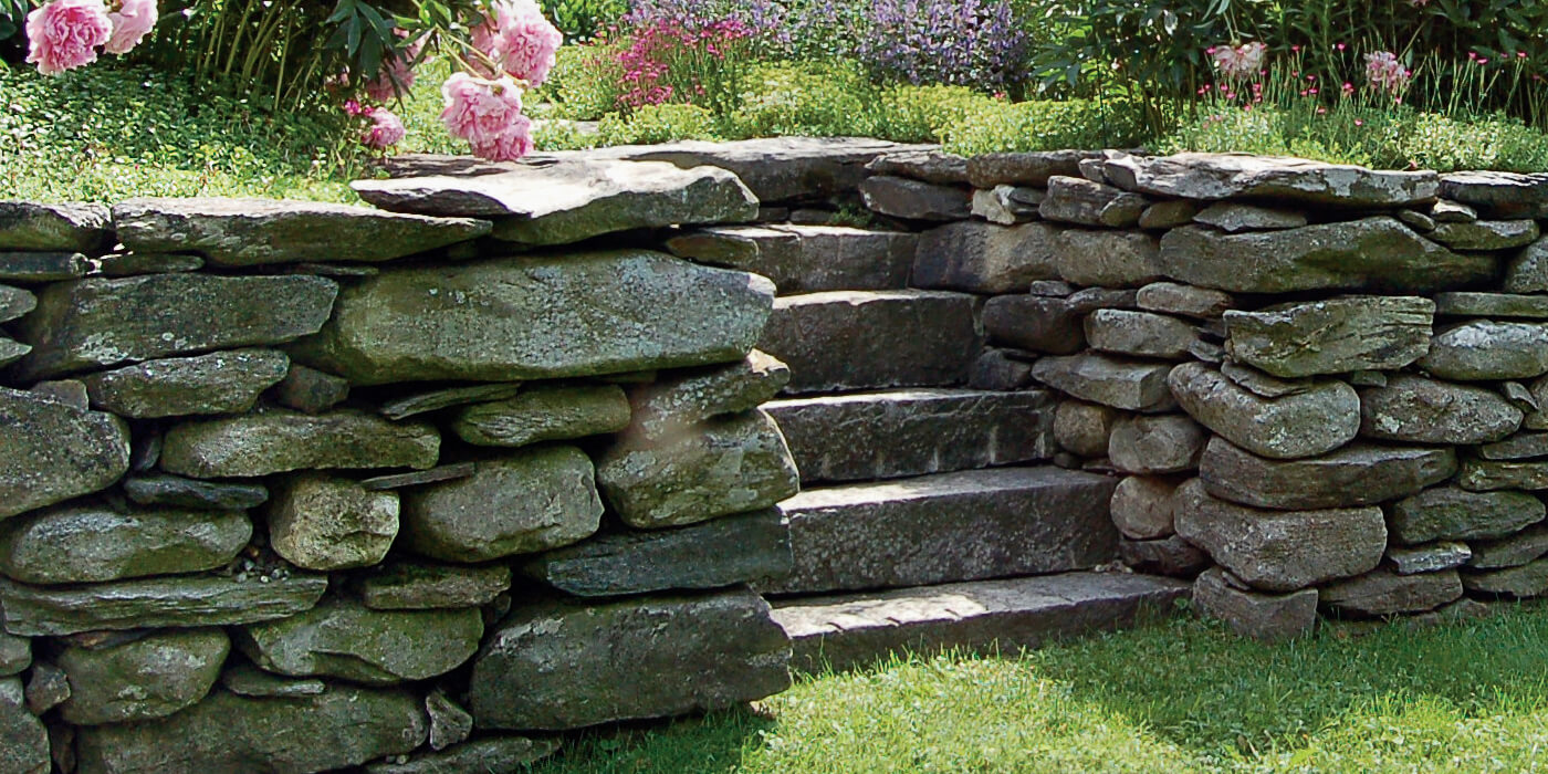 Stone wall and stairs leading up to a garden.
